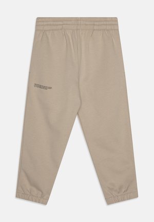 Pantalones jogger beige fabricados con algodón orgánico. Cuentan con una cintura elástica, dobladillos acampanados y un pequeño detalle de texto impreso en el lado izquierdo.
