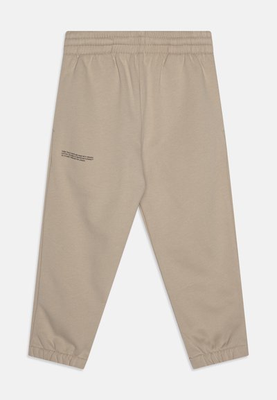 Pantalones jogger beige fabricados con algodón orgánico. Cuentan con una cintura elástica, dobladillos acampanados y un pequeño detalle de texto impreso en el lado izquierdo.
