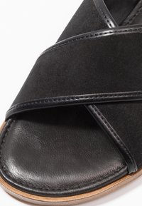 Black slide sandal featuring a cross strap design, made of suede and leather. Textured sole with a smooth leather finish.