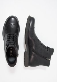 Botas de cuero negro con detalles de brogue, punta redonda, cordones en la parte frontal y cremallera lateral. Suela de goma resistente con un ligero relieve.