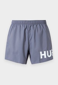 Γκρι ανδρικό μαγιό με ελαστική μέση και μερική λευκή επιγραφή "HUG" στο κάτω δεξί πόδι, σε λευκό φόντο.