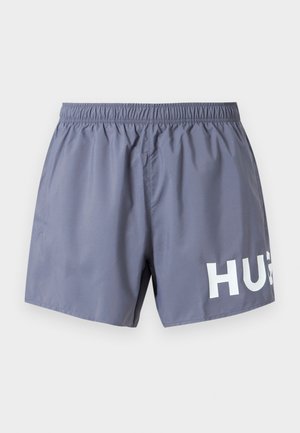 Sivé pánske plavecké šortky s elastickým pásom a čiastočným bielym nápisom "HUG" na spodnej pravej nohe na bielom pozadí.