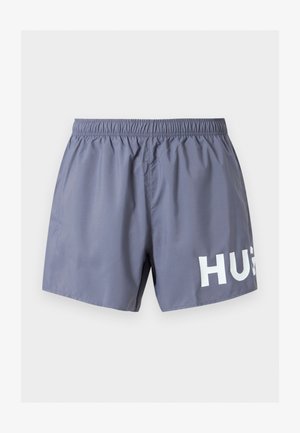 Halli meeste ujumispüksid elastse vöökohaga ja osaliselt valge "HUG" tekst alumise parema jala juures valge tausta kõrval.