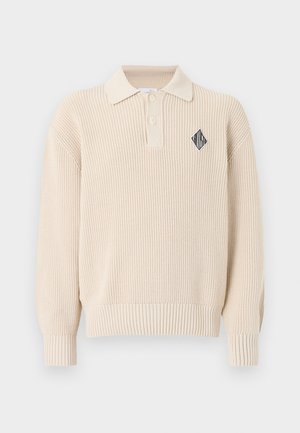 Pull polo beige en maille à manches longues avec poignets et ourlet côtelés, deux boutons, et un petit logo en forme de losange noir et blanc sur la poitrine.