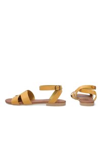 Žluté kožené sandály s křížovými pásky a přezkou na kotníku. Plochá podrážka s hnědým stélkou a minimalistický design. Styl s otevřenou špičkou.