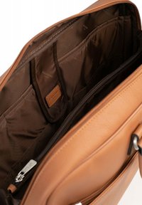 Interieur van een tan leren messenger bag, met een donkerbruine voering, meerdere compartimenten, ritssluiting en een leren label met merklogo.
