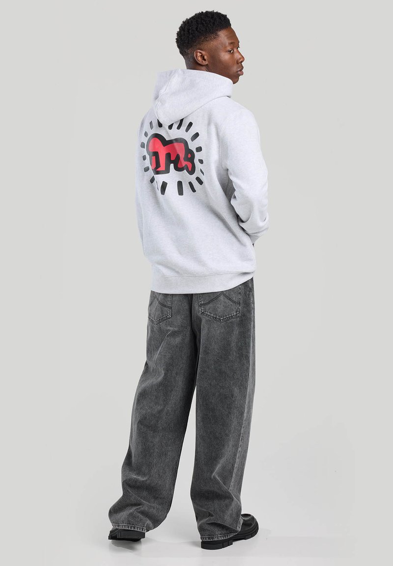 Gray hoodie with large red and black graphic on the back, worn with loose-fitting gray pants and black footwear. Minimalist design.