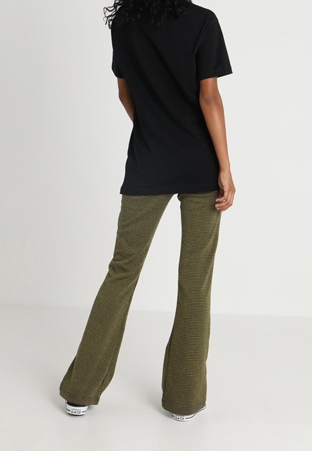 Černé bavlněné tričko s krátkým rukávem spárované s olivově zelenými károvanými rozšířenými kalhotami. Oblečení doplňují bílé tenisky.