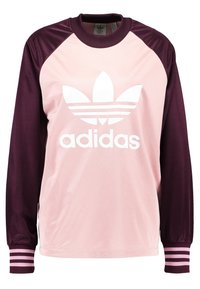 Adidas långärmad tröja i rosa och vinröd. Mjukt tyg, raglanärmar, vitt logo fram, randiga manschetter, design med rundad halsringning.