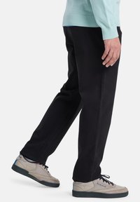 Zwarte broek met een rechte pasvorm, gemaakt van een gladde stof, gecombineerd met lichtgrijze sneakers met blauwe accenten.
