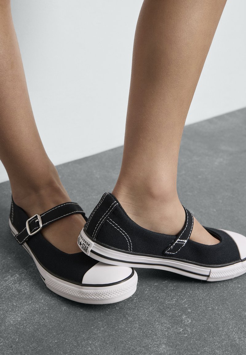 Zapatillas de lienzo negras con un diseño de Mary Jane, que cuentan con una correa con hebilla, una puntera de goma blanca y detalles de costura en contraste.