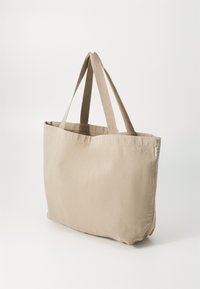 Beige Canvas Tragetasche aus robustem Stoff, flacher Form und langen Stoffgriffen. Enthält ein dezentes Reißverschlussdetail auf einer Seite.