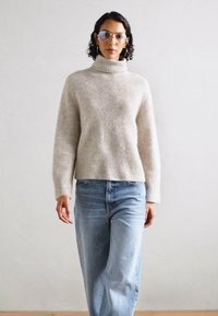 Lys grå, ribbet høyhalset genser kombinert med høytlivede, lyseblå denimjeans. Glatt tekstur, avslappet passform, med minimalistisk design.