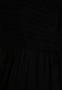 Černé šaty s nabíraným živůtkem a skládanou sukní. Vyrobené z lehkého materiálu, mají jemnou texturu a podrobnosti s vodorovným prošíváním.