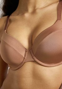 Reggiseno imbottito marrone realizzato in tessuto liscio. Presenta spalline regolabili, una forma arrotondata e dettagli cuciti al centro e ai bordi.