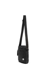 Čierna crossbody taška vyrobená z hladkého syntetického materiálu. Má nastaviteľný popruh, zipsové priehradky a malý kovový logo akcent.