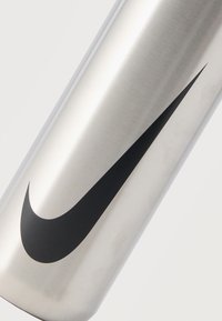 Κυλινδρικό αντικείμενο από ανοξείδωτο ατσάλι με μεγάλο μαύρο λογότυπο Nike swoosh στην επιφάνειά του ενάντια σε λευκό φόντο.