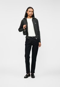 Mørk grå zip-up jakke, hvit topp, mørke jeans, svarte loafers og liten svart veske; har en slank passform og minimalistisk design.