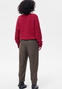 Czerwony sweter z dzianiny z teksturowanymi rękawami, zestawiony z brązowymi spodniami we wzory oraz czarnymi botkami z srebrnymi ozdobami.