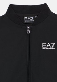 Bomber nero con colletto alto, chiusura frontale con zip e logo EA7 Emporio Armani. Realizzato in tessuto liscio e leggero.