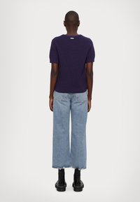 Tmavě fialový pletený top s krátkými rukávy a kulatým výstřihem, doplněný světle modrými širokými džínami a černými kotníkovými botami.