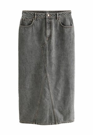 Kobieta w beżowym bezrękawnym topie typu crop oraz wysokim, szarym dżinsowym maxi spódnicy, stojąca boso na tle w kolorze szarym.