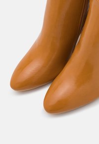 Botas de tobillo de cuero marrón con punta afilada y textura suave, con una cremallera lateral para el cierre y un detalle de costura minimalista.
