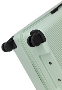 Valigia rigida di colore verde menta con superficie testurizzata, doppie ruote nere e chiusura a zip. Presenta bordi arrotondati e dettagli robusti.