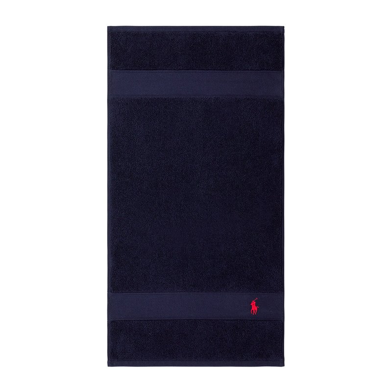 Πετσέτα από βαμβάκι σε σκούρο μπλε χρώμα με υφή, που διαθέτει οριζόντια ρίγα και μικρό κόκκινο λογότυπο στο κάτω μέρος. Παραλληλόγραμμο σχήμα.