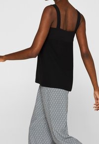 Musta tank top leveillä olkaimilla ja suoralinjaisella leikkauksella; yhdistetty harmaisiin, hienovaraisella ympyräkuvioinnilla varustettuihin housuihin.