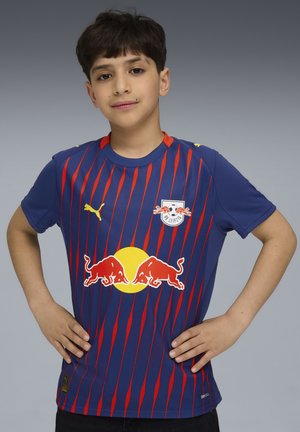 Maillot de sport rayé rouge et bleu avec un col rond, affichant un grand cercle jaune et un logo de taureau rouge sur le devant, et le logo Puma sur la manche.