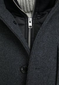 Cappotto di lana grigio con chiusura a bottoni e cerniera argentata. Presenta una fodera trapuntata nera e un colletto interno a coste grigio.