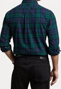 Grün und marineblau karierter Flanellhemd mit langen Ärmeln, Knopfkragen und aufgerollten Manschetten. Kombiniert mit schwarzen Denim-Hosen.