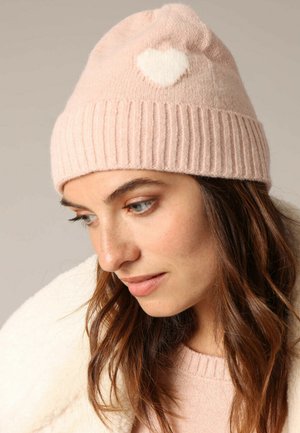 Bonnet en tricot rose clair avec une texture côtelée, présentant un accent en feutre blanc en forme de cœur sur le devant. Matériau doux en mélange de laine.