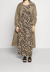 Khaki trench coat přes maxi šaty s leopardím potiskem v béžové barvě s černými a hnědými skvrnami. Černé skluzavkové sandály s robustními podrážkami.