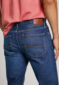 Vaqueros de mezclilla de un azul oscuro con un corte clásico, dos bolsillos traseros y un parche de cuero de la marca en la cinturilla. Detalles de costura sutil.