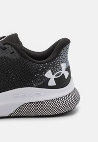 Schwarzer Sportschuh mit einem strukturierten Mesh-Obermaterial, geformtem Fersenbereich, weißem HOVR-Logo und einer gepunkteten weißen Außensohle für besseren Halt.
