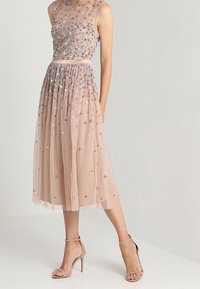 Vestido midi de tul suave en color melocotón con cuentas, que presenta un corsé ajustado y una falda plisada. Con acentos de lentejuelas coloridas por todo el vestido, combinado con tacones nude.