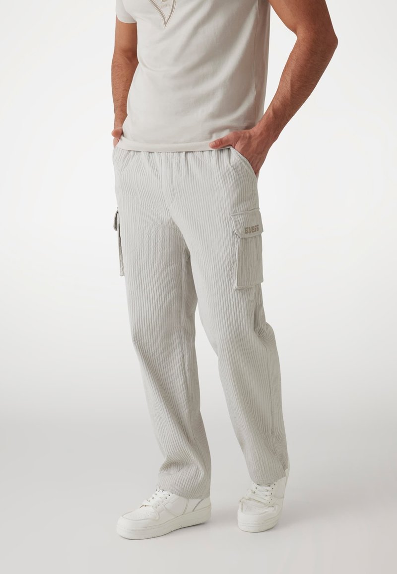Ljusgrå ribbade cargo-byxor med elastisk midja, sidofickor och GUESS-logotyp på fickan. Matchat med vita sneakers.
