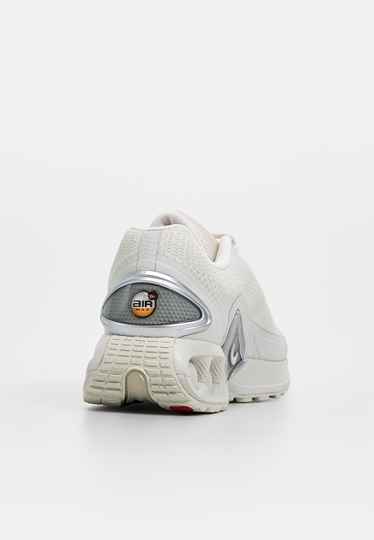 Beżowe buty sportowe z teksturowaną cholewką, srebrnymi akcentami i wyraźnym logo Air Max. Posiadają rzeźbioną podeszwę i gumowy bieżnik.