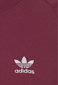 Mörkröd sweatshirt med ribbat mönster, med en vit broderad Adidas-logotyp och tre ränder. Rundhalsad design, figurnära stil.