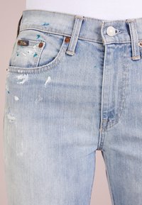 Světle modré denimové džíny s malými skvrnami od barvy, štítek Polo na kapsičce a kovové zapínání na knoflík.