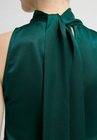 Zelený saténový top bez rukávů s vysokým límcem a detaily uvázanými vzadu, s hladkou texturou a jemným leskem.