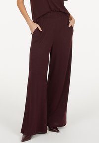 Burgundy wide-leg pants with a stretchy waistband, two side pockets, and a soft, smooth texture. Paired with pointed-toe shoes.