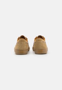 Tan suede skate shoes with a textured back, orange accents, and a rubber sole. Features stitched logo and heel tab for easy wear.