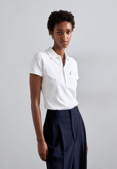 White polo shirt with a collared neckline and short sleeves, featuring a small logo on the left chest. Paired with navy wide-leg trousers.