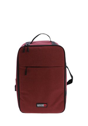 Mochila de tela roja con forma cuadrada, que cuenta con un bolsillo frontal con cremallera, detalles en negro y un asa superior para un transporte fácil.