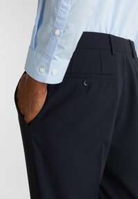 Ljusblå skjorta med knappar och mörkblå skräddarsydda byxor. Byxorna har en bakficka med knapp och en slät yta.