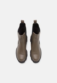 Un par de botas Chelsea de cuero color topo con paneles laterales elásticos negros y lengüetas, vistas desde arriba sobre un fondo blanco.
