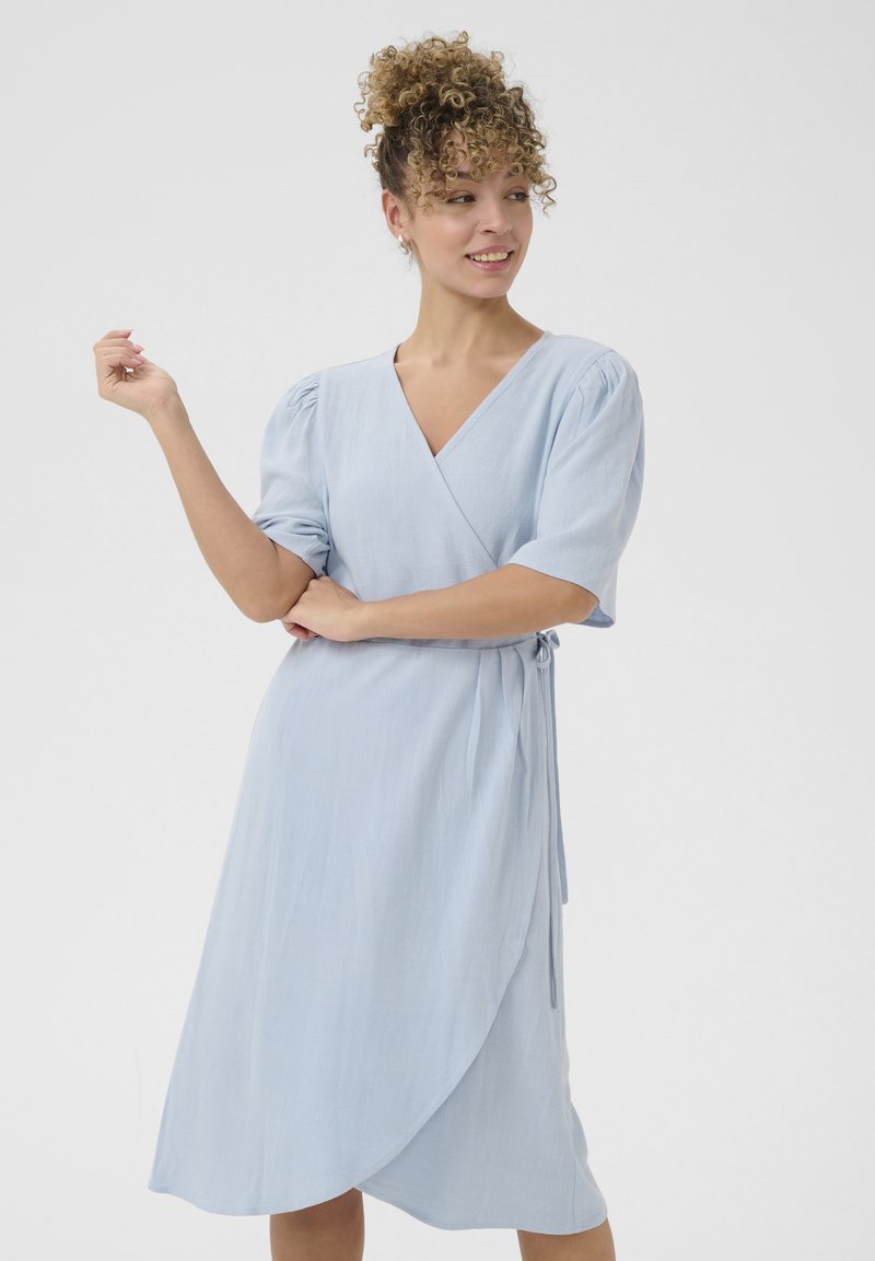 Abito avvolgente azzurro chiaro realizzato in un tessuto morbido e textured. Presenta un collo a V, maniche corte a sbuffo e una cintura da legare in vita.
